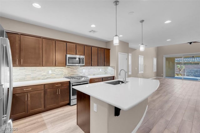 kitchen with pendant lighting, sink, decorative backsplash, a kitchen island with sink, and stainless steel appliances