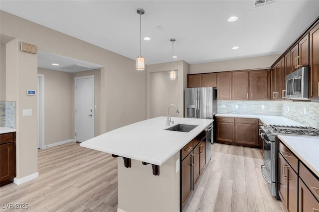 kitchen with sink, tasteful backsplash, decorative light fixtures, a center island with sink, and stainless steel appliances