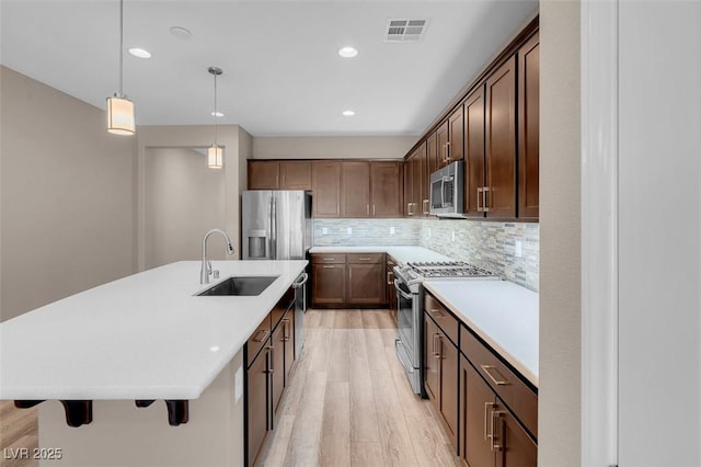 kitchen featuring appliances with stainless steel finishes, decorative light fixtures, sink, a kitchen breakfast bar, and a center island with sink