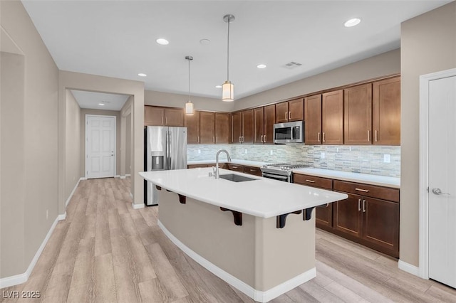 kitchen featuring sink, appliances with stainless steel finishes, a kitchen breakfast bar, pendant lighting, and a kitchen island with sink