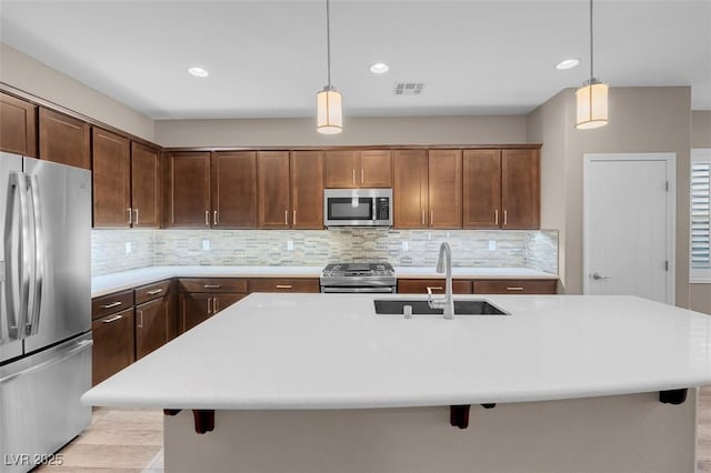 kitchen with appliances with stainless steel finishes, sink, a center island with sink, and decorative light fixtures