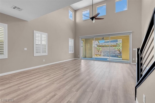 unfurnished living room featuring a high ceiling, ceiling fan, and light wood-type flooring