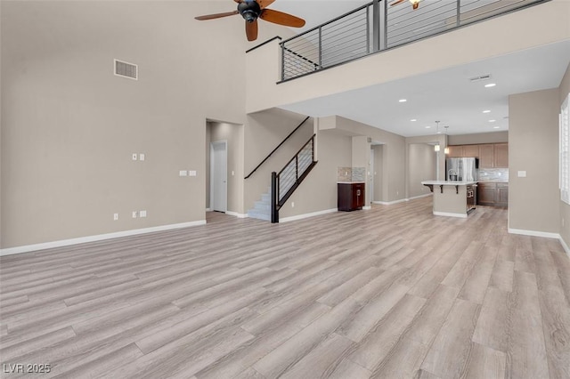 unfurnished living room with ceiling fan, light hardwood / wood-style flooring, and a towering ceiling