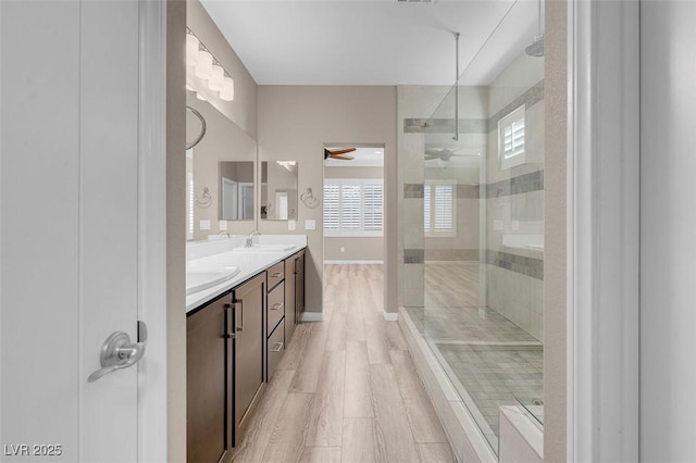 bathroom with hardwood / wood-style flooring, ceiling fan, vanity, and a tile shower