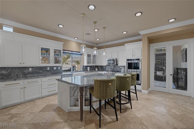 kitchen featuring appliances with stainless steel finishes, white cabinetry, hanging light fixtures, dark stone countertops, and a center island with sink