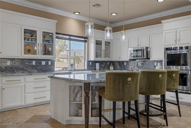 kitchen with a breakfast bar area, appliances with stainless steel finishes, light stone counters, white cabinets, and a kitchen island