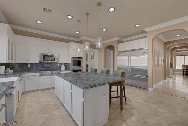 kitchen featuring stainless steel appliances, white cabinetry, a center island, and dark stone countertops