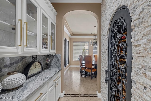 bar featuring light tile patterned floors, crown molding, tasteful backsplash, light stone countertops, and white cabinets