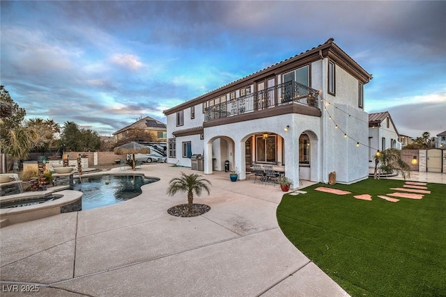 back house at dusk featuring a swimming pool with hot tub, a yard, a patio, and a balcony