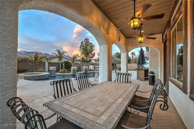 patio terrace at dusk featuring pool water feature, ceiling fan, a swimming pool with hot tub, and a mountain view