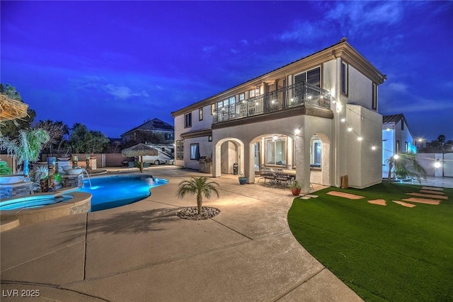 back house at dusk with a patio, a balcony, a lawn, a swimming pool with hot tub, and pool water feature