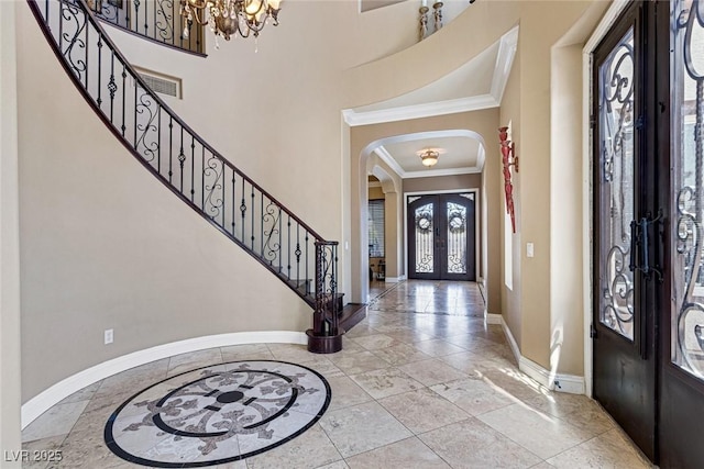 foyer featuring ornamental molding, a towering ceiling, an inviting chandelier, and french doors