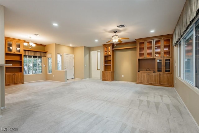 unfurnished living room featuring built in shelves, light colored carpet, and ceiling fan with notable chandelier