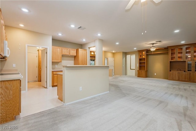 kitchen featuring ceiling fan, light colored carpet, and light brown cabinets