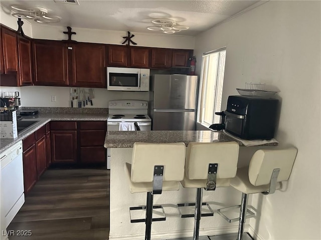 kitchen featuring dark hardwood / wood-style flooring, sink, white appliances, and a breakfast bar area