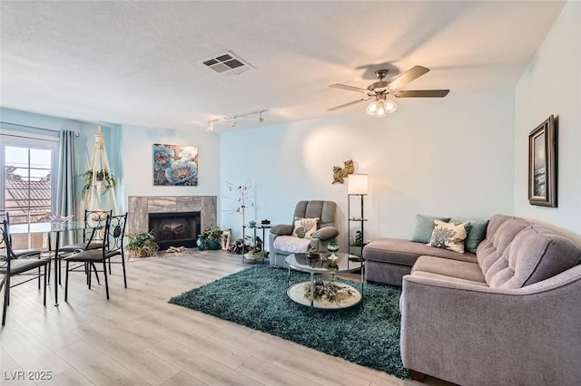 living room with wood-type flooring, ceiling fan, a high end fireplace, track lighting, and a textured ceiling