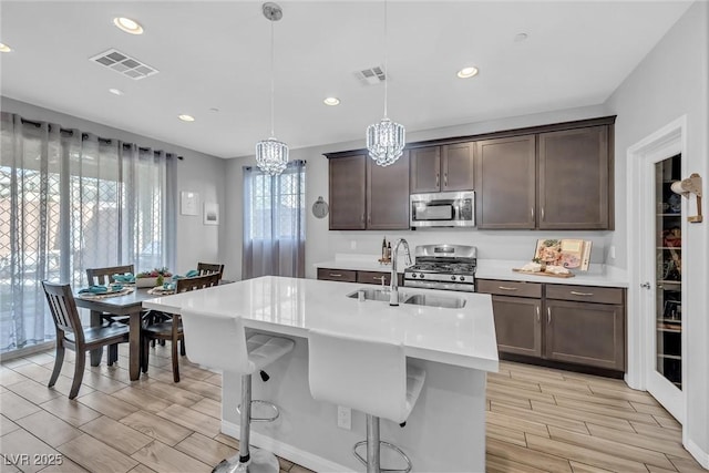 kitchen with dark brown cabinetry, a breakfast bar area, decorative light fixtures, an island with sink, and stainless steel appliances