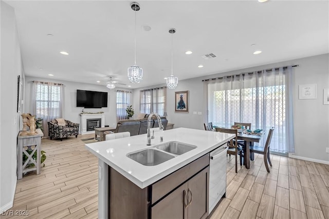 kitchen with sink, dishwasher, ceiling fan, an island with sink, and decorative light fixtures