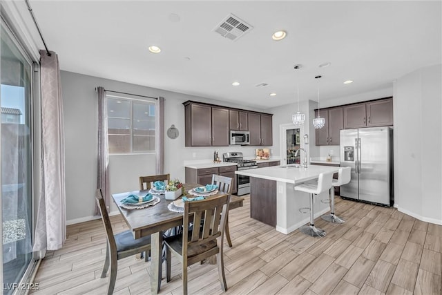 kitchen featuring pendant lighting, sink, dark brown cabinetry, stainless steel appliances, and a center island with sink