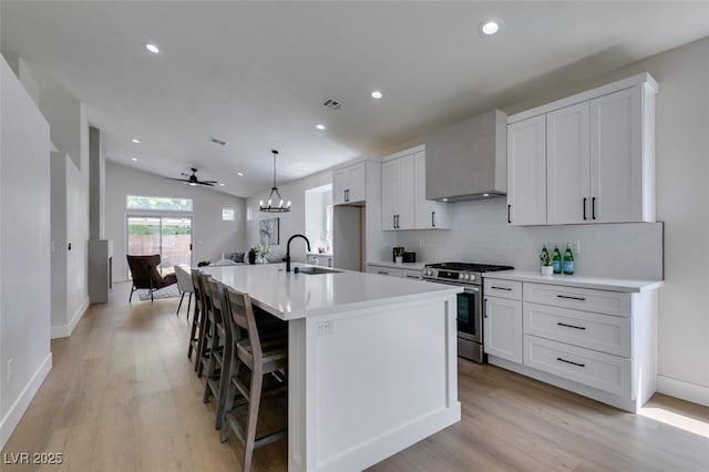 kitchen featuring sink, stainless steel gas stove, decorative light fixtures, an island with sink, and wall chimney range hood