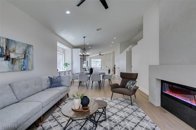 living room with ceiling fan with notable chandelier and light wood-type flooring