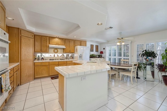 kitchen with sink, tile countertops, light tile patterned floors, a raised ceiling, and white appliances