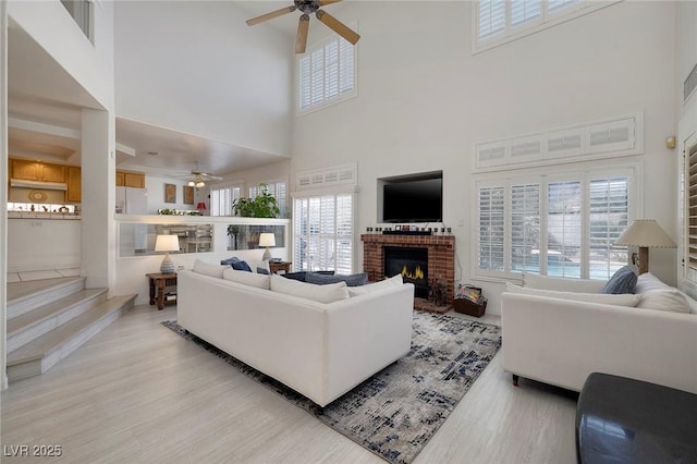 living room with ceiling fan, a towering ceiling, a fireplace, and light hardwood / wood-style floors