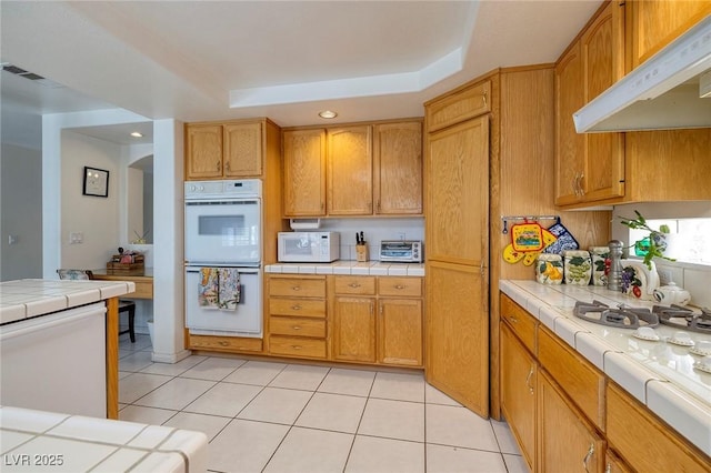 kitchen with tile countertops, white appliances, and a tray ceiling