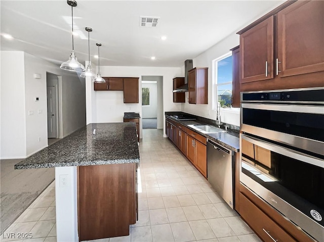 kitchen featuring stainless steel appliances, a kitchen island, sink, dark stone counters, and wall chimney range hood