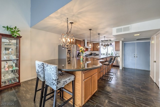 kitchen with stainless steel refrigerator with ice dispenser, decorative light fixtures, wall chimney range hood, and a spacious island