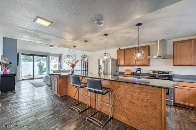 kitchen with pendant lighting, wall chimney range hood, a breakfast bar area, and stainless steel appliances