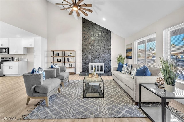 living room with a fireplace, high vaulted ceiling, ceiling fan, and light wood-type flooring