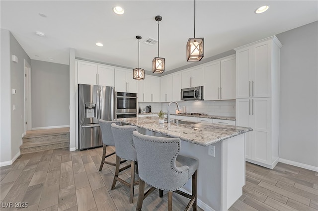 kitchen featuring sink, stainless steel appliances, an island with sink, and white cabinets