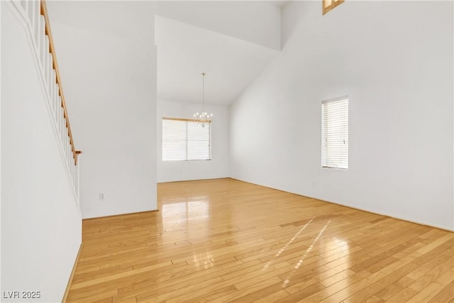 empty room featuring a notable chandelier, a towering ceiling, and light wood-type flooring