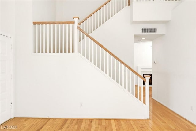 stairway with wood-type flooring, a tile fireplace, and a high ceiling