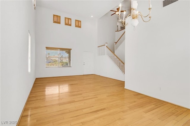 unfurnished living room featuring a towering ceiling, a chandelier, and light wood-type flooring