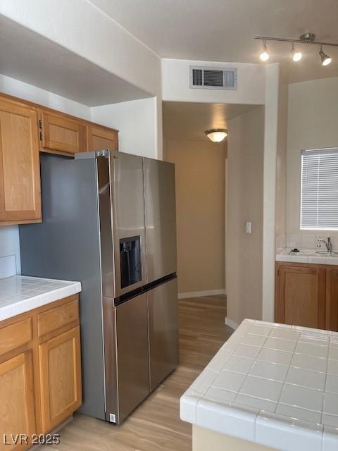 kitchen with sink, tile counters, light hardwood / wood-style floors, and stainless steel refrigerator with ice dispenser