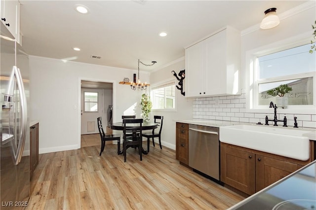 kitchen with sink, appliances with stainless steel finishes, decorative backsplash, white cabinets, and decorative light fixtures