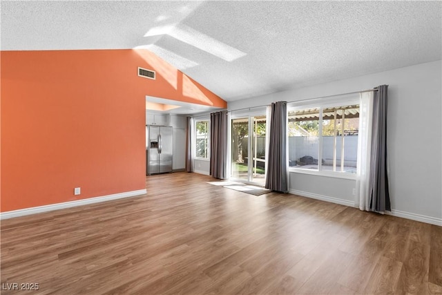 unfurnished room with hardwood / wood-style flooring, lofted ceiling with skylight, and a textured ceiling