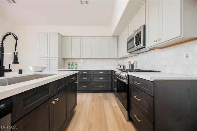 kitchen with appliances with stainless steel finishes, white cabinetry, sink, decorative backsplash, and light wood-type flooring