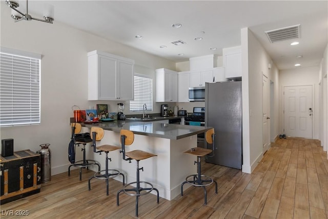 kitchen featuring appliances with stainless steel finishes, a breakfast bar, white cabinets, light hardwood / wood-style floors, and kitchen peninsula