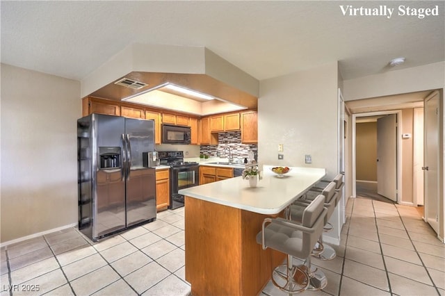 kitchen featuring tasteful backsplash, a peninsula, light tile patterned flooring, visible vents, and black appliances