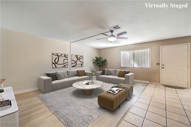 living room featuring visible vents, a ceiling fan, light wood-style floors, and a textured ceiling