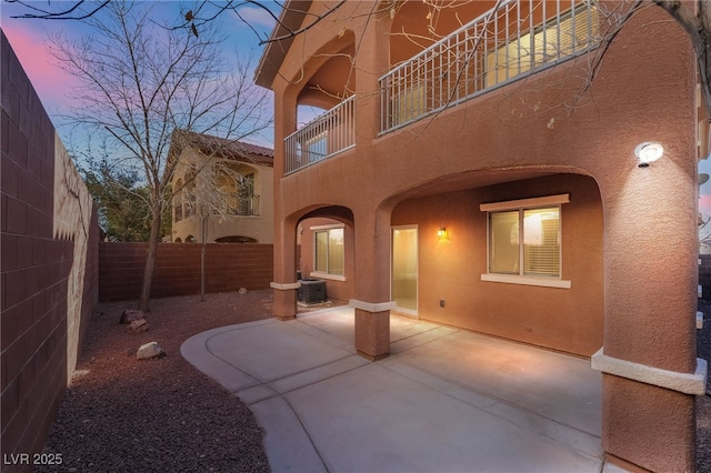 patio terrace at dusk featuring cooling unit and a balcony