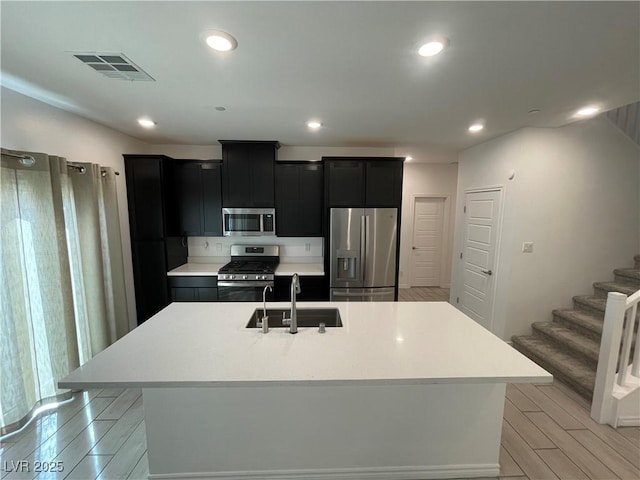 kitchen featuring appliances with stainless steel finishes, sink, a kitchen island with sink, and light hardwood / wood-style flooring