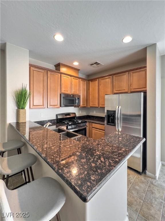 kitchen with stainless steel appliances, a breakfast bar, a peninsula, brown cabinets, and dark stone counters