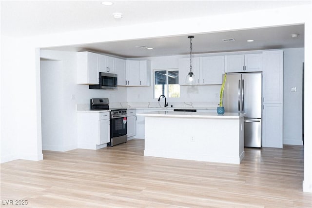 kitchen featuring pendant lighting, stainless steel appliances, white cabinets, and a kitchen island