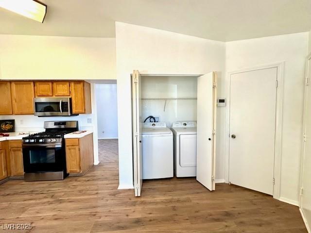 kitchen featuring appliances with stainless steel finishes, washing machine and clothes dryer, and light wood-type flooring