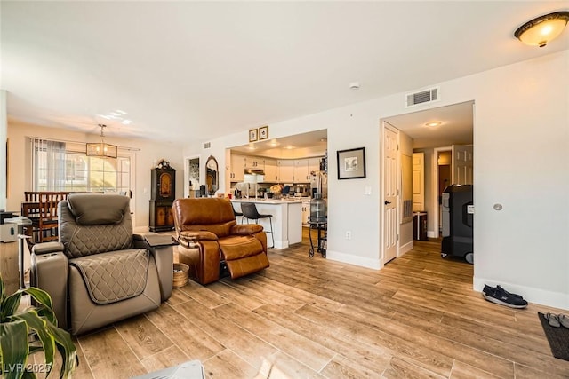 living area with a notable chandelier, visible vents, light wood-type flooring, and baseboards