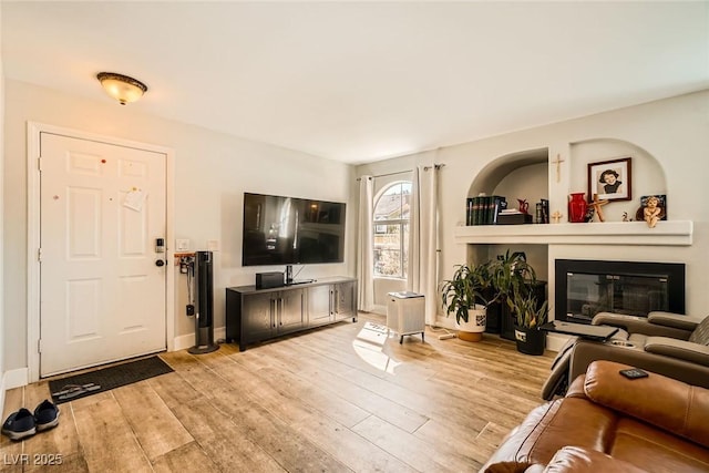 living room with a glass covered fireplace, baseboards, and light wood finished floors